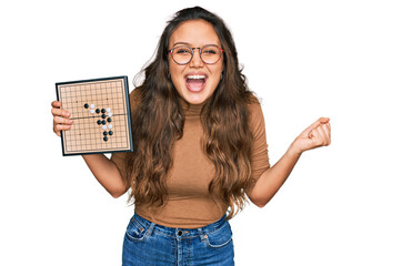 Young hispanic girl holding drauhgts screaming proud, celebrating victory and success very excited...
