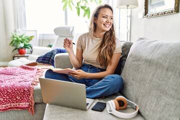 Young hispanic girl having online class sitting on the sofa at home.