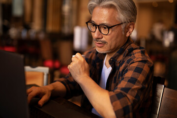 Businessman working on laptop in cafe. Handsome senior man enjoying in fresh coffee.
