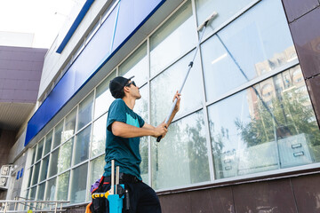 Male professional cleaning service worker in overalls cleans the windows and shop windows of a...