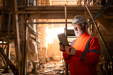 Portrait of miner in safety uniform, hardhat and lamp standing inside underground mine and checking...