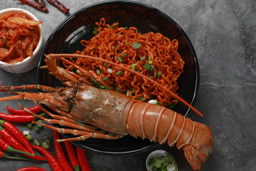 Top view Korean spicy dried instant noodle with painted spiny lobster and kimchi on black table...
