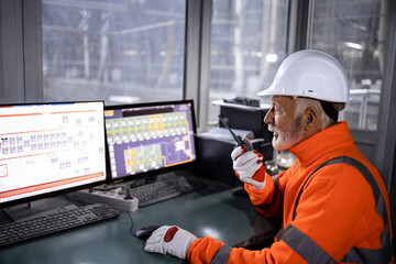 Industrial worker in safety equipment sitting in factory control room monitoring production process...
