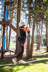 Child using safety equipment at adventure amusement park. Young girl having fun outdoor. Childhood active. Sports extreme activity.