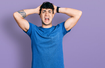 Young hispanic man wearing casual t shirt crazy and scared with hands on head, afraid and surprised of shock with open mouth