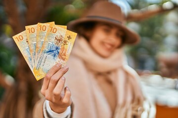 Young hispanic woman wearing elegant style holding swiss franc banknotes at the city.