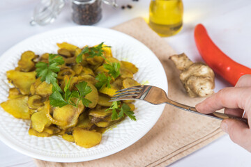 A woman's hand with a fork over a plate of fried jerusalem artichoke.