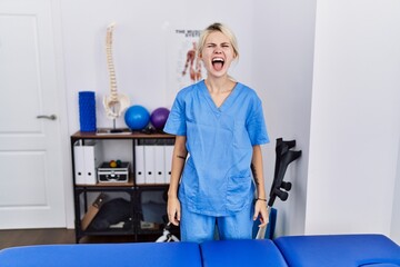 Young physiotherapist woman working at pain recovery clinic angry and mad screaming frustrated and furious, shouting with anger. rage and aggressive concept.