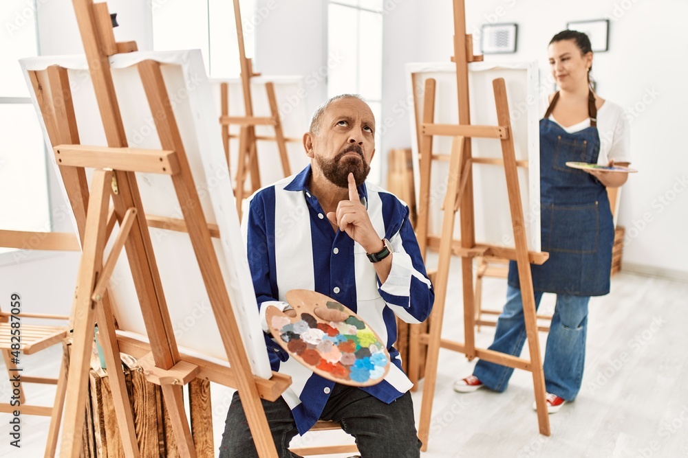 Canvas Prints Senior artist man at art studio thinking concentrated about doubt with finger on chin and looking up wondering