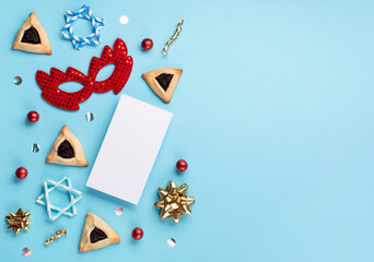 Purim celebration jewish carnival holiday concept. Tasty hamantaschen cookies, red carnival mask, noisemaker, sweet candies and party decor on blue background. Top view, flat lay, copy space.