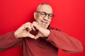 Fototapeta premium Handsome mature man wearing casual sweater and glasses smiling in love doing heart symbol shape with hands. romantic concept.