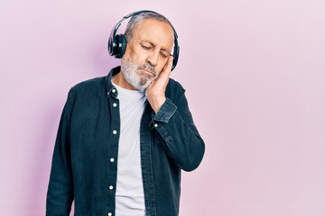 Handsome senior man with beard listening to music using headphones thinking looking tired and bored with depression problems with crossed arms.