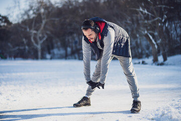 Fototapeta na wymiar Adult man is exercising in park in wintertime. He is stretching his body before jogging.