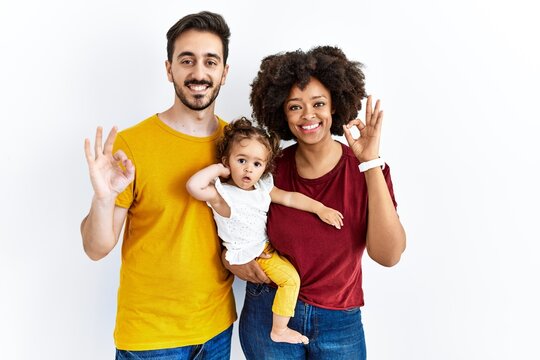 Interracial Young Family Of Black Mother And Hispanic Father With Daughter Smiling Positive Doing Ok Sign With Hand And Fingers. Successful Expression.