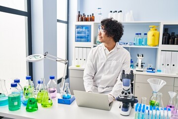 Young hispanic man wearing scientist uniform using laptop at laboratory
