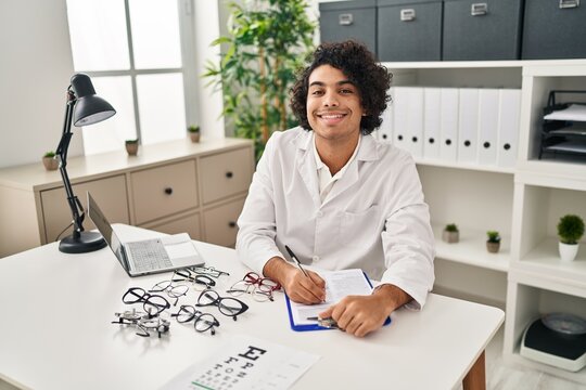 Young hispanic man optician writing on clipboard at clinic