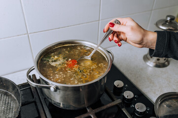 The girl, the cook prepares a soup from vegetables in boiling water, stirring the water in a saucepan with a spoon. Food preparation.