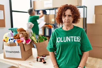 Middle age woman wearing volunteer t shirt at donations stand skeptic and nervous, frowning upset because of problem. negative person.