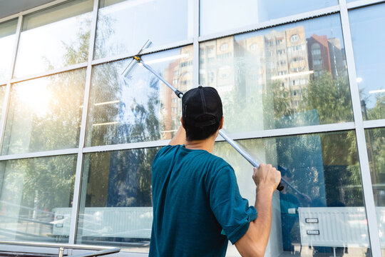 Male professional cleaning service worker in overalls cleans the windows and shop windows of a store with special equipment