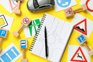 Many different road signs, notebook with sketch of roundabout and toy car on yellow background,...