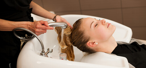 Hair stylist at work - hairdresser washing hair to the customer before doing hairstyle in a professional salon