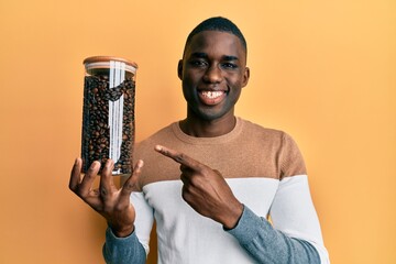 Young african american man holding jar with coffee beans smiling happy pointing with hand and finger