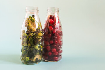 The concept of using fast-freezing products. Frozen green vegetables and red berries with ice crystals in transparent bottles on a light background.
