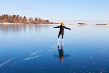 A young athletic girl is skating on the transparent ice of the frozen Lake Baikal. Transparent ice,...