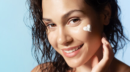 Pretty  girl with heart shaped face cream or foam on cheek, healthy skin, smiling during daily...