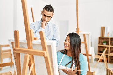 Fototapeta na wymiar Young latin painter couple smiling happy painting at art studio