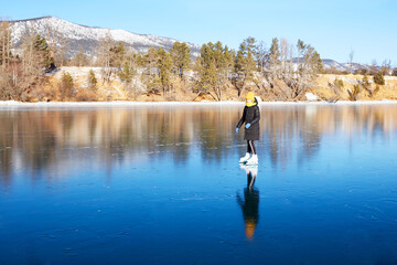 A young athletic girl is skating on the transparent ice of the frozen Lake Baikal on a sunny winter day. The concept of active winter recreation and sports. 