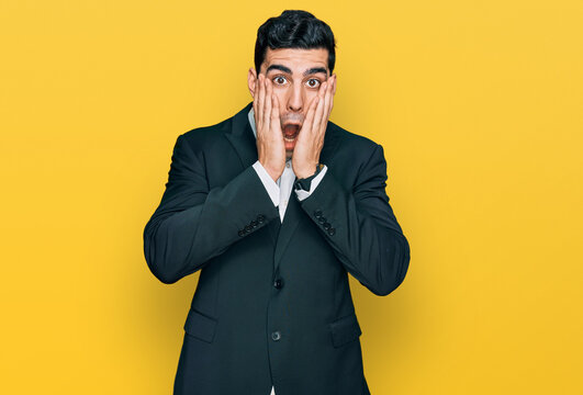 Handsome hispanic man wearing business clothes afraid and shocked, surprise and amazed expression with hands on face