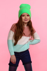 Naklejka premium a girl in a striped sweater and a bright green cap poses in the studio on a pink background