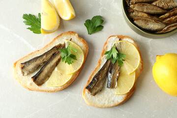 Sandwiches with sprats and ingredients on light background