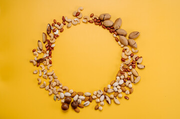 Mix of different types of dried nuts in compositions on a yellow background. Top view. Flat lay