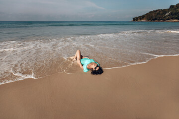 Fototapeta na wymiar Sexy tanned slim woman in bikini lying on the sea coast. Woman in beachwear swimsuit lying on wet sand of beach. Summertime recreation and travel concept.