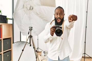 African american photographer man working at photography studio pointing displeased and frustrated to the camera, angry and furious with you