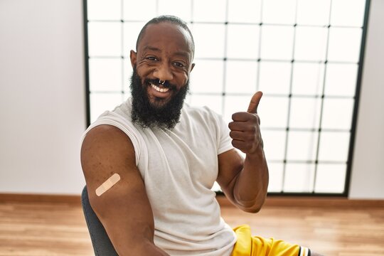 African american man getting vaccine showing arm with band aid smiling happy and positive, thumb up doing excellent and approval sign