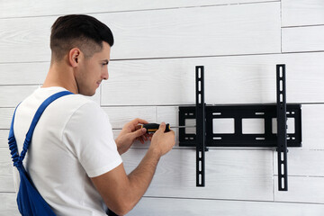Professional technician with screwdriver installing TV bracket on wall indoors - obrazy, fototapety, plakaty