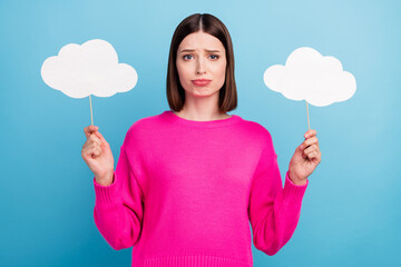 Photo of upset charming young woman dressed pink sweater holding two mind clouds empty space isolated blue color background