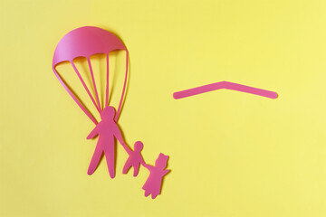 Abstract painting of three cardboard people an adult and two children flying on a parachute and a red roof.