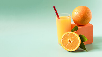 Banner natural orange juice in a transparent glass with a decor of oranges and green leaves on a light green background.