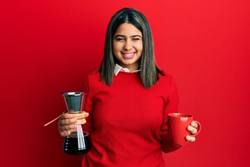 Young latin woman holding coffee filter and cup winking looking at the camera with sexy expression,...