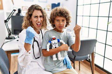 Young kid at pediatrician clinic holding teddy bear annoyed and frustrated shouting with anger,...