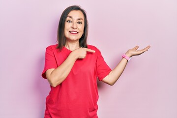 Middle age hispanic woman wearing casual clothes amazed and smiling to the camera while presenting with hand and pointing with finger.