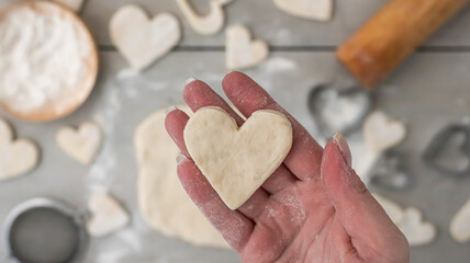 Hand holds heart cut from dough. Cooking gingerbread cookies for the holidays: christmas, new year,...