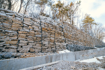 Stone gabion wall along the asphalt road in winter