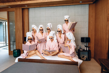Group of adorable focused female models in the same clothes wearing bathrobes, a towel on their heads and sunglasses and posing with a menu in their hands indoor. Self-care concept