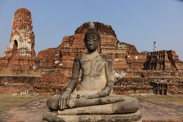 Buddha statue at Wat Mahathat with small black pot resting on its leg and the ruins in the background (horizontal image), Ayutthaya, Thailand