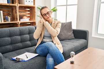 Young woman working at consultation office sleeping tired dreaming and posing with hands together while smiling with closed eyes.